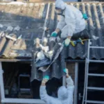 due addetti attrezzati di dispositivi di sicurezza rimuovono delle lastre di eternit da un tetto