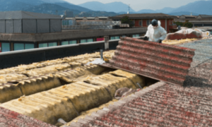 1 addetto alla rimozione di eternit sono posizionati su un tetto per bonificare l'area con appositi dispositivi ed attrezzi di sicurezza
